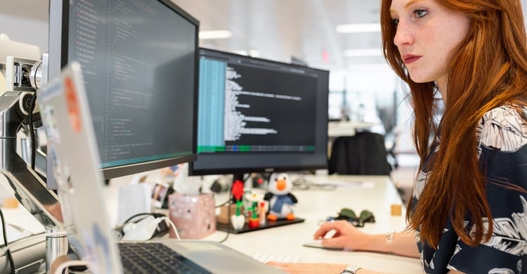 Female employee reviewing data on computer monitors for SOC 2 compliance