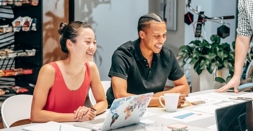 Smiling coworkers at desk reviewing essential background check results on laptop